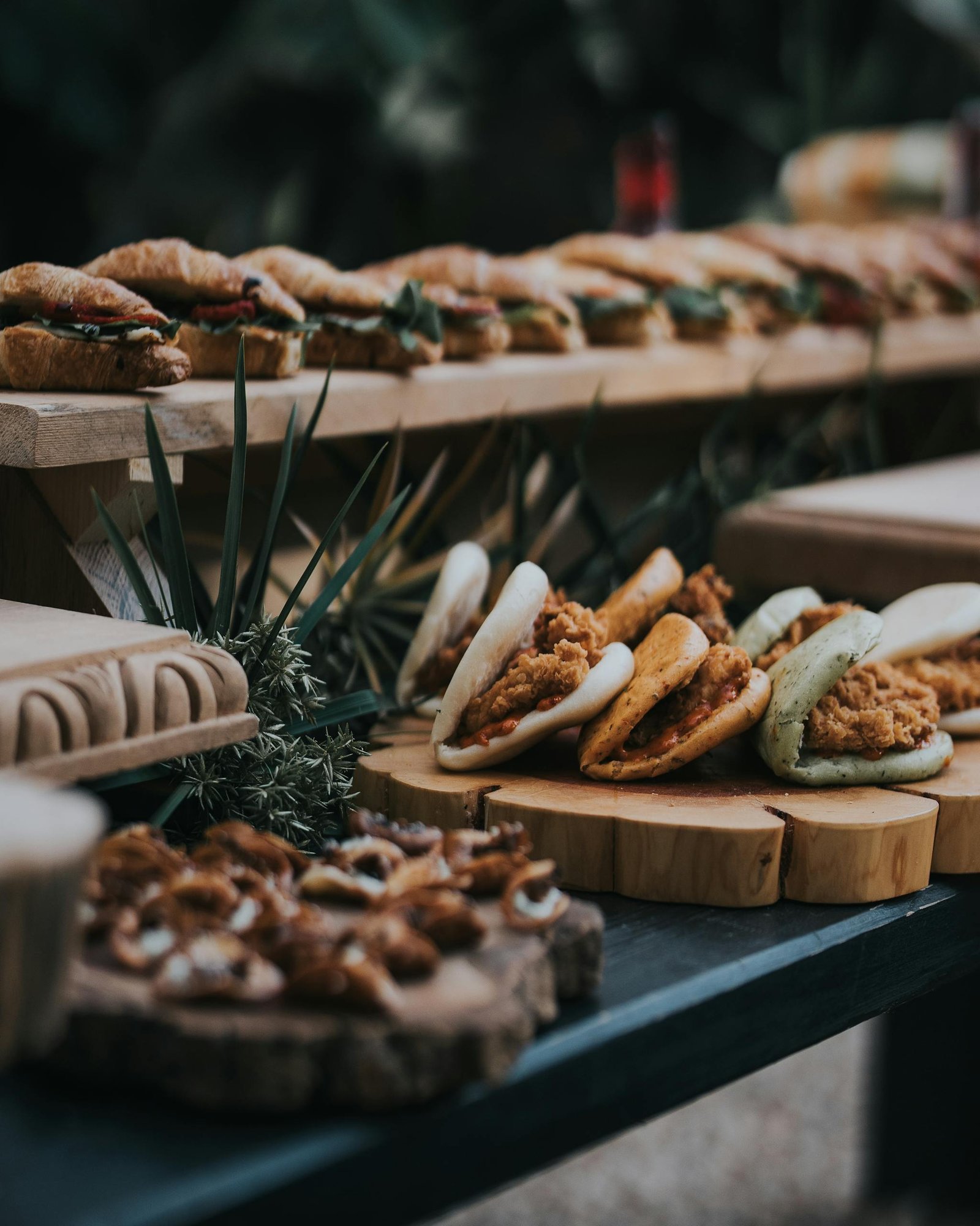 A variety of gourmet sandwiches displayed on rustic wooden platters at an outdoor event.
